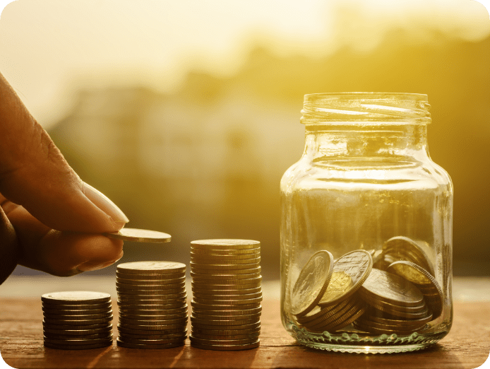 A person arranging coins in stacks with a coin jar next to him during sunset