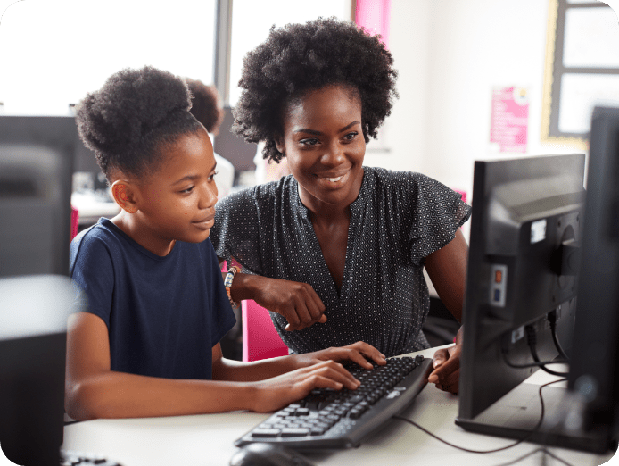 Lady and young girl looking at desktop as the young girl keys on the keyboard