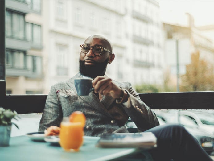 A fine looking polished man holding a cup outdoors with his pad on the table