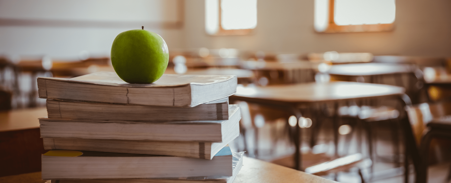 Green apple on top of a pile of books in an empty classroom